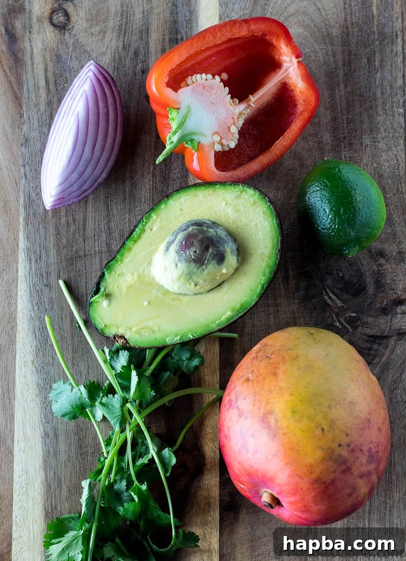 Red onion, red bell pepper, lime, avocado, cilantro, and mango on a chopping board.