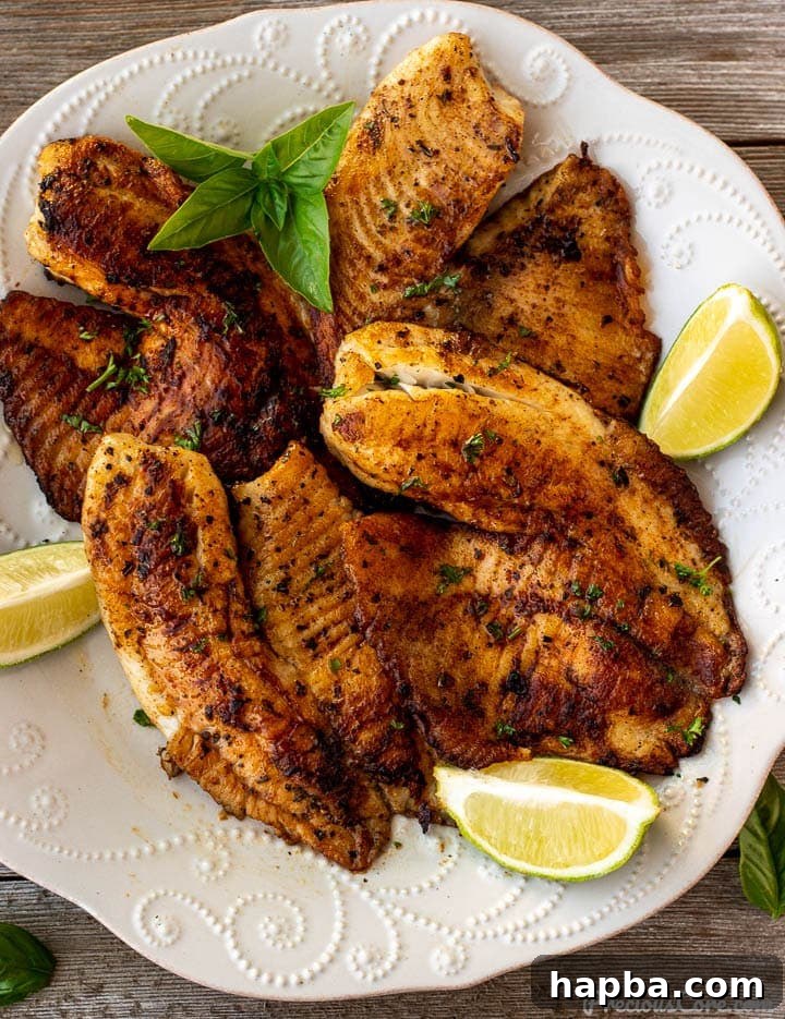 Golden Seared Tilapia 2 Golden Pan Seared Tilapia on a plate, garnished with fresh lime wedges, ready to be served.