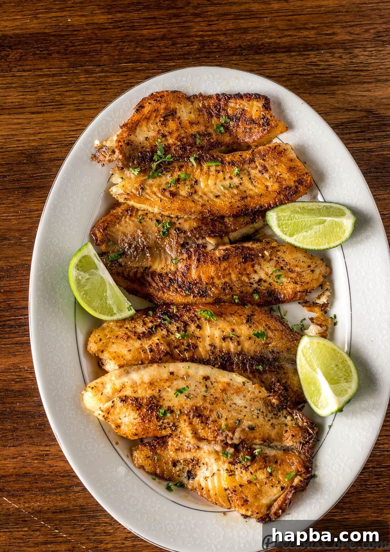 Golden Seared Tilapia 7 Pan Seared Tilapia fillets beautifully arranged on a serving tray, accompanied by fresh lime wedges for squeezing.