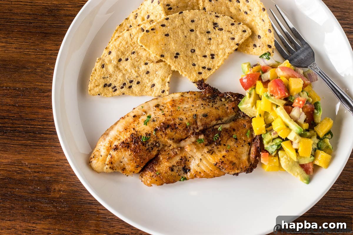 Golden Seared Tilapia 8 A plate of Pan Seared Tilapia served with a colorful Mango Avocado Salsa and crispy tortilla chips, creating a vibrant and delicious meal.