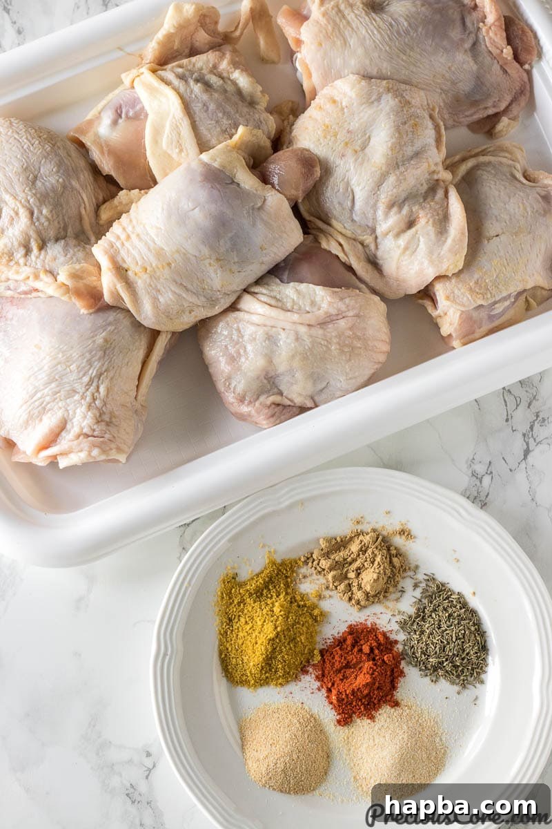 Dry rub ingredients laid out on a plate next to raw chicken thighs on a baking tray.