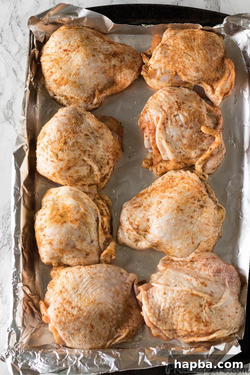 Raw chicken thighs on a baking sheet, generously coated with a savory dry rub.