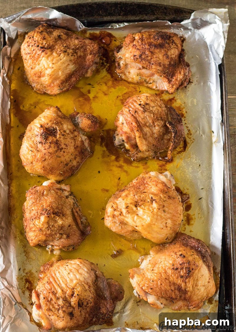 Freshly baked golden brown chicken thighs cooling on a baking sheet, skin perfectly crispy.