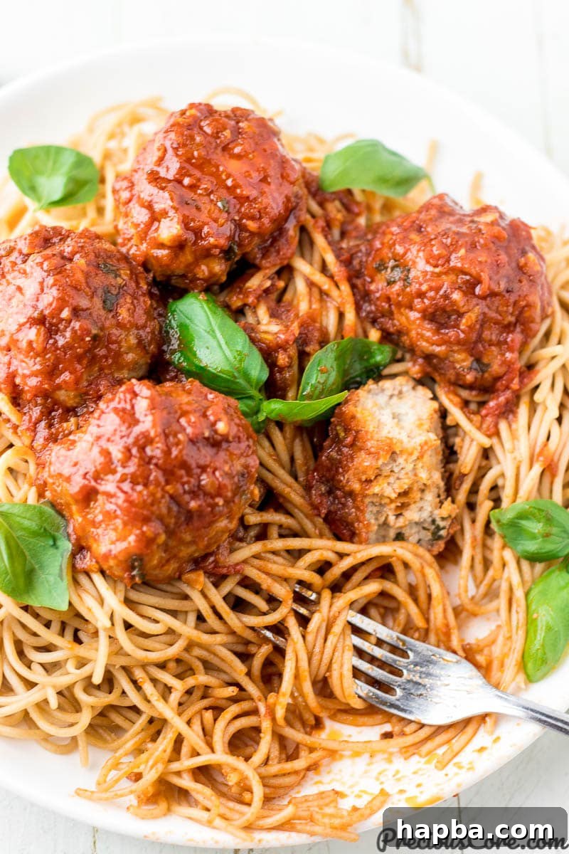 Classic chicken meatballs with spaghetti, garnished with fresh herbs.