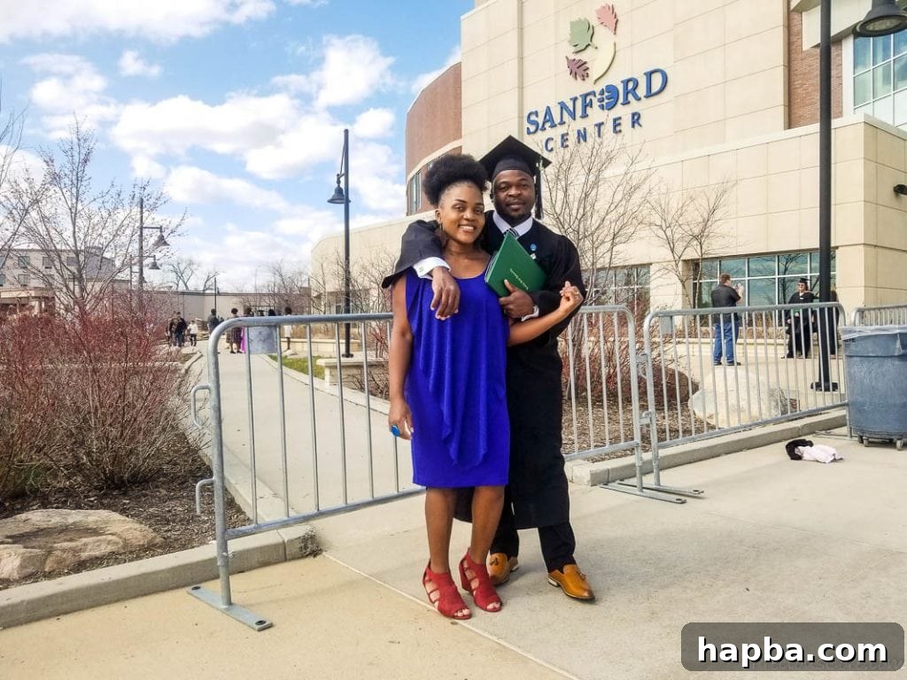 Man in graduation gear with a woman in a blue dress in front of the Sanford Center.
