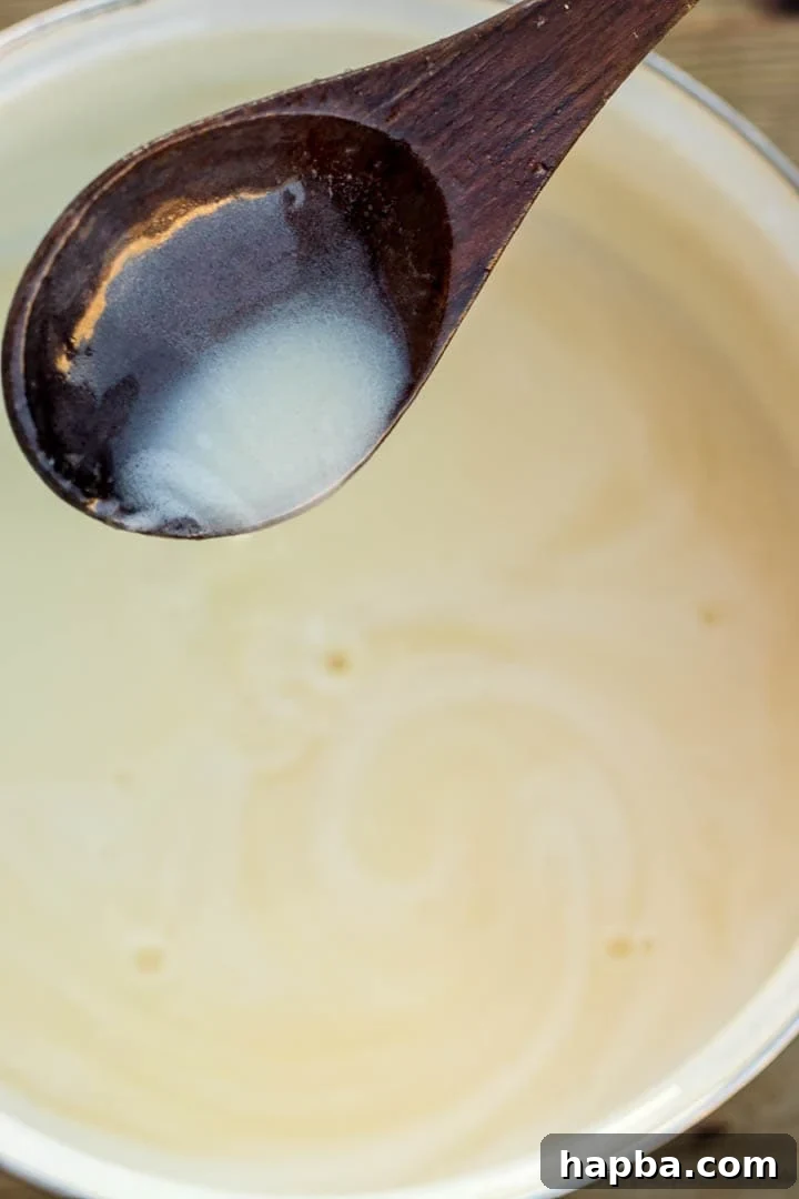 Decadent Bread Pudding Drizzle 7 A spoon gracefully pouring the warm, glistening Bread Pudding Sauce, showcasing its smooth and inviting consistency.