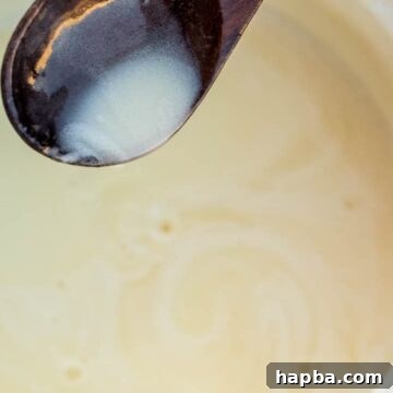 A spoon pouring creamy Bread Pudding Sauce over a dessert