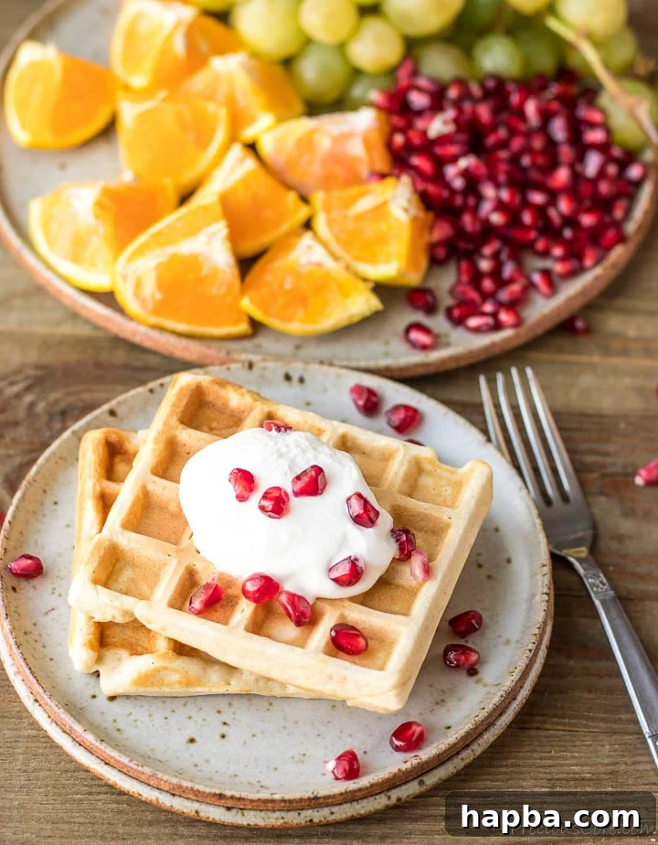 Waffle Perfection from Your Kitchen 3 Two golden brown waffles on a plate, generously topped with whipped cream and vibrant pomegranate seeds.