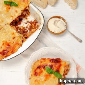 Slice of Lasagna on a plate with a bowl of freshly baked lasagna on the side.