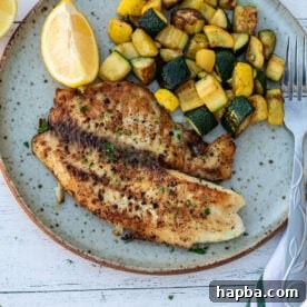 Lemon pepper tilapia on a plate with sautéed zucchini.