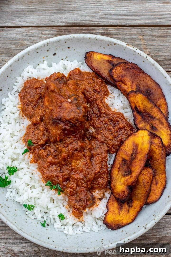 A serving of African chicken stew gracefully placed over a mound of white rice.